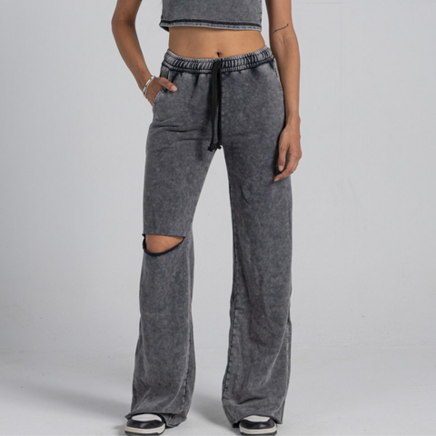 Model wearing the BROWNTOAST ASSID Women’s Sweatpants from the ASSID Kollection — relaxed-fit cotton-blend sweatpants with a ripped knee detail, adjustable waist, and unique dye variations. Made in Egypt for a lived-in, one-of-a-kind streetwear look.