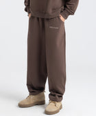 Model wearing the BROWNTOAST Core Barrel Sweats from the Core Drop — unisex cotton sweatpants in coffee brown with a relaxed barrel-shaped leg, elastic waistband, and side pockets. Made in Egypt for structured comfort and clean everyday style.