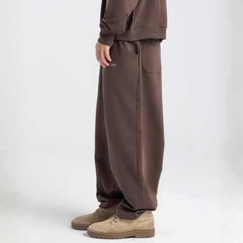 Model wearing the BROWNTOAST Core Barrel Sweats from the Core Drop — unisex cotton sweatpants in coffee brown with a relaxed barrel-shaped leg, elastic waistband, and side pockets. Made in Egypt for structured comfort and clean everyday style.