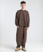 Model wearing the BROWNTOAST Core Barrel Sweats from the Core Drop — unisex cotton sweatpants in coffee brown with a relaxed barrel-shaped leg, elastic waistband, and side pockets. Made in Egypt for structured comfort and clean everyday style.