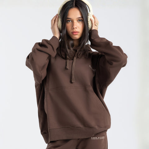 Model wearing the BROWNTOAST Core Hoodie from the Core Drop in coffee brown — a relaxed unisex hoodie with an adjustable drawstring hood, kangaroo pocket, and front silk-screen print. Made in Egypt from a soft cotton blend for an elevated everyday look.