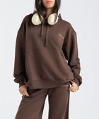 Model wearing the BROWNTOAST Core Hoodie from the Core Drop in coffee brown — a relaxed unisex hoodie with an adjustable drawstring hood, kangaroo pocket, and front silk-screen print. Made in Egypt from a soft cotton blend for an elevated everyday look.