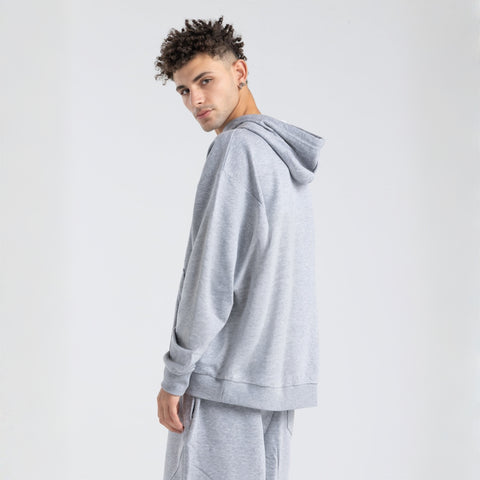 Model wearing the BROWNTOAST Core Hoodie from the Core Drop in light grey— a relaxed unisex hoodie with an adjustable drawstring hood, kangaroo pocket, and front silk-screen print. Made in Egypt from a soft cotton blend for an elevated everyday look.