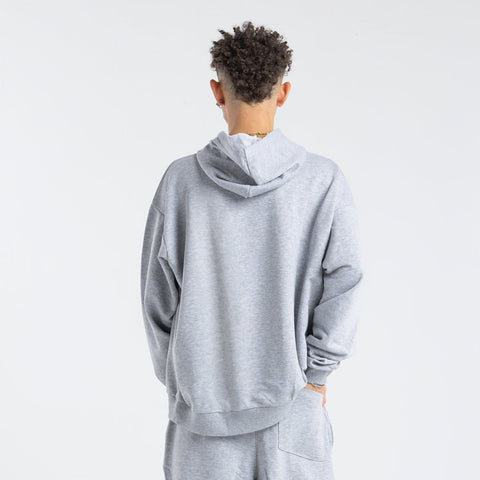 Model wearing the BROWNTOAST Core Hoodie from the Core Drop in light grey— a relaxed unisex hoodie with an adjustable drawstring hood, kangaroo pocket, and front silk-screen print. Made in Egypt from a soft cotton blend for an elevated everyday look.