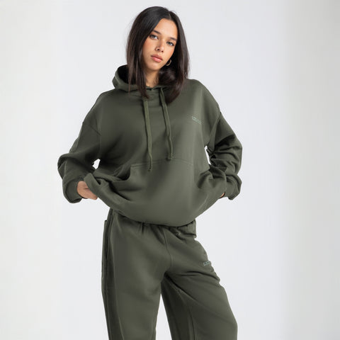  Model wearing the BROWNTOAST Core Hoodie from the Core Drop in olive green— a relaxed unisex hoodie with an adjustable drawstring hood, kangaroo pocket, and front silk-screen print. Made in Egypt from a soft cotton blend for an elevated everyday look.