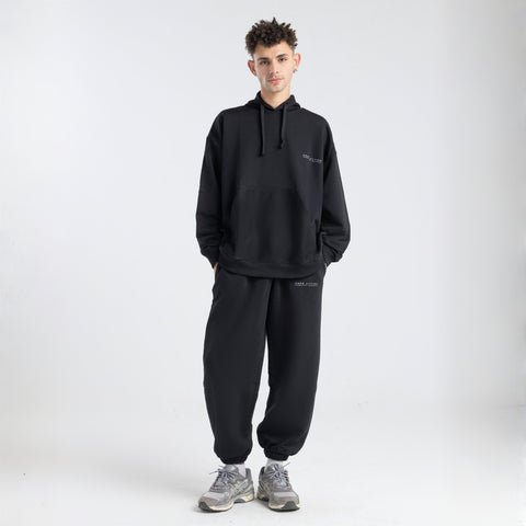 Model wearing the BROWNTOAST Core Hoodie from the Core Drop in black— a relaxed unisex hoodie with an adjustable drawstring hood, kangaroo pocket, and front silk-screen print. Made in Egypt from a soft cotton blend for an elevated everyday look.