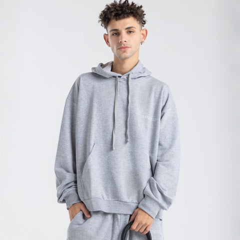 Model wearing the BROWNTOAST Core Hoodie from the Core Drop in light grey— a relaxed unisex hoodie with an adjustable drawstring hood, kangaroo pocket, and front silk-screen print. Made in Egypt from a soft cotton blend for an elevated everyday look.