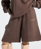 Model wearing the BROWNTOAST Core Long Shorts from the Core Drop in coffee brown — relaxed unisex cotton-lycra shorts with front piping detail, side pockets, and an adjustable drawstring waist. Knee-length design balancing bermuda and short fit, made in Egypt for everyday comfort and style.