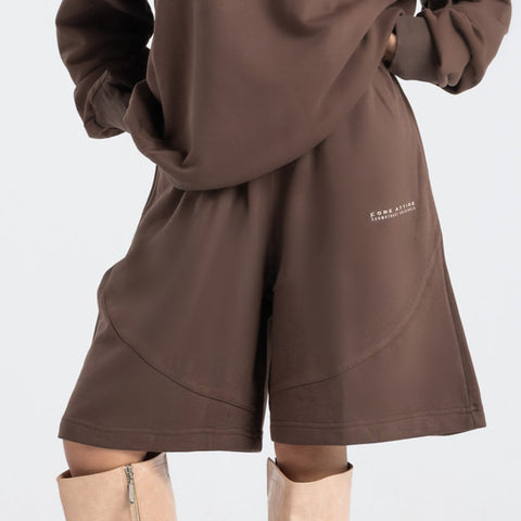 Model wearing the BROWNTOAST Core Long Shorts from the Core Drop in coffee brown — relaxed unisex cotton-lycra shorts with front piping detail, side pockets, and an adjustable drawstring waist. Knee-length design balancing bermuda and short fit, made in Egypt for everyday comfort and style.