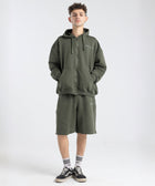 Model wearing the BROWNTOAST Core Long Shorts from the Core Drop in olive green — relaxed unisex cotton-lycra shorts with front piping detail, side pockets, and an adjustable drawstring waist. Knee-length design balancing bermuda and short fit, made in Egypt for everyday comfort and style.