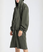 Model wearing the BROWNTOAST Core Long Shorts from the Core Drop in olive green — relaxed unisex cotton-lycra shorts with front piping detail, side pockets, and an adjustable drawstring waist. Knee-length design balancing bermuda and short fit, made in Egypt for everyday comfort and style.