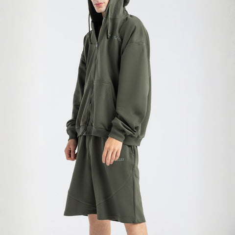 Model wearing the BROWNTOAST Core Long Shorts from the Core Drop in olive green — relaxed unisex cotton-lycra shorts with front piping detail, side pockets, and an adjustable drawstring waist. Knee-length design balancing bermuda and short fit, made in Egypt for everyday comfort and style.