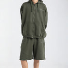 Model wearing the BROWNTOAST Core Long Shorts from the Core Drop in olive green — relaxed unisex cotton-lycra shorts with front piping detail, side pockets, and an adjustable drawstring waist. Knee-length design balancing bermuda and short fit, made in Egypt for everyday comfort and style.