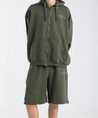 Model wearing the BROWNTOAST Core Long Shorts from the Core Drop in olive green — relaxed unisex cotton-lycra shorts with front piping detail, side pockets, and an adjustable drawstring waist. Knee-length design balancing bermuda and short fit, made in Egypt for everyday comfort and style.