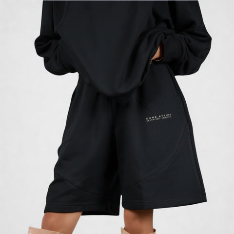 Model wearing the BROWNTOAST Core Long Shorts from the Core Drop in black — relaxed unisex cotton-lycra shorts with front piping detail, side pockets, and an adjustable drawstring waist. Knee-length design balancing bermuda and short fit, made in Egypt for everyday comfort and style.