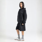 Model wearing the BROWNTOAST Core Long Shorts from the Core Drop in black — relaxed unisex cotton-lycra shorts with front piping detail, side pockets, and an adjustable drawstring waist. Knee-length design balancing bermuda and short fit, made in Egypt for everyday comfort and style.