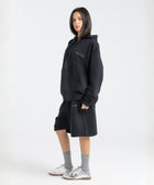 Model wearing the BROWNTOAST Core Long Shorts from the Core Drop in black — relaxed unisex cotton-lycra shorts with front piping detail, side pockets, and an adjustable drawstring waist. Knee-length design balancing bermuda and short fit, made in Egypt for everyday comfort and style.