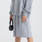 Model wearing the BROWNTOAST Core Long Shorts from the Core Drop in light grey — relaxed unisex cotton-lycra shorts with front piping detail, side pockets, and an adjustable drawstring waist. Knee-length design balancing bermuda and short fit, made in Egypt for everyday comfort and style.