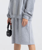 Model wearing the BROWNTOAST Core Long Shorts from the Core Drop in light grey — relaxed unisex cotton-lycra shorts with front piping detail, side pockets, and an adjustable drawstring waist. Knee-length design balancing bermuda and short fit, made in Egypt for everyday comfort and style.