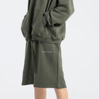 Model wearing the BROWNTOAST Core Long Shorts from the Core Drop in olive green — relaxed unisex cotton-lycra shorts with front piping detail, side pockets, and an adjustable drawstring waist. Knee-length design balancing bermuda and short fit, made in Egypt for everyday comfort and style.