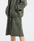 Model wearing the BROWNTOAST Core Long Shorts from the Core Drop in olive green — relaxed unisex cotton-lycra shorts with front piping detail, side pockets, and an adjustable drawstring waist. Knee-length design balancing bermuda and short fit, made in Egypt for everyday comfort and style.