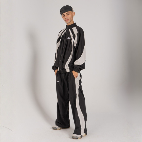 Model wearing the BROWNTOAST Compton Tracksuit Pants — unisex oversized polyester track pants inspired by old-school Compton style and 80s hip-hop culture. Features adjustable waist and BTO rubber and embroidered logos. Available in black and white.