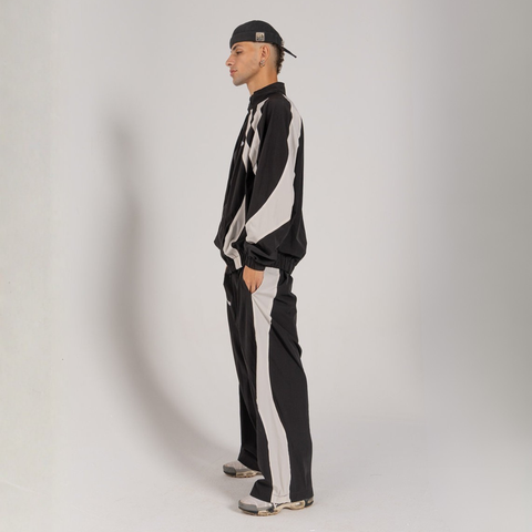 Model wearing the BROWNTOAST Compton Tracksuit Pants — unisex oversized polyester track pants inspired by old-school Compton style and 80s hip-hop culture. Features adjustable waist and BTO rubber and embroidered logos. Available in black and white.