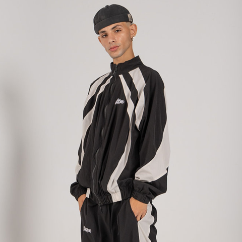 Model wearing the BROWNTOAST Compton Tracksuit Jacket — unisex oversized polyester track jacket with a dual-function zipper and BTO rubber and embroidered logos. Inspired by old-school Compton style and 80s hip-hop culture. Available in black and white.