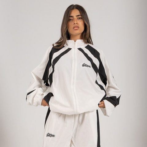 Model wearing the BROWNTOAST Compton Tracksuit Jacket — unisex oversized polyester track jacket with a dual-function zipper and BTO rubber and embroidered logos. Inspired by old-school Compton style and 80s hip-hop culture. Available in black and white.