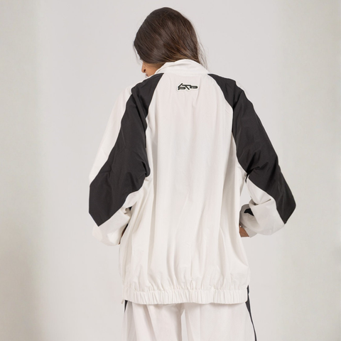 Model wearing the BROWNTOAST Compton Tracksuit Jacket — unisex oversized polyester track jacket with a dual-function zipper and BTO rubber and embroidered logos. Inspired by old-school Compton style and 80s hip-hop culture. Available in black and white.