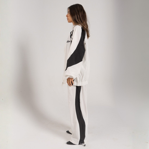 Model wearing the BROWNTOAST Compton Tracksuit Jacket — unisex oversized polyester track jacket with a dual-function zipper and BTO rubber and embroidered logos. Inspired by old-school Compton style and 80s hip-hop culture. Available in black and white.