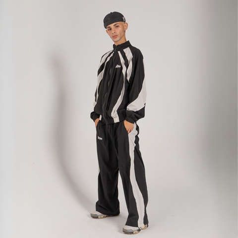 Model wearing the BROWNTOAST Compton Tracksuit Jacket — unisex oversized polyester track jacket with a dual-function zipper and BTO rubber and embroidered logos. Inspired by old-school Compton style and 80s hip-hop culture. Available in black and white.