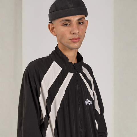 Model wearing the BROWNTOAST Compton Tracksuit Jacket — unisex oversized polyester track jacket with a dual-function zipper and BTO rubber and embroidered logos. Inspired by old-school Compton style and 80s hip-hop culture. Available in black and white.