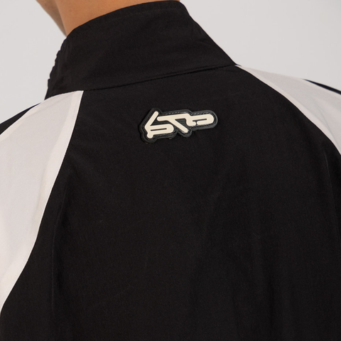 Model wearing the BROWNTOAST Compton Tracksuit Jacket — unisex oversized polyester track jacket with a dual-function zipper and BTO rubber and embroidered logos. Inspired by old-school Compton style and 80s hip-hop culture. Available in black and white.