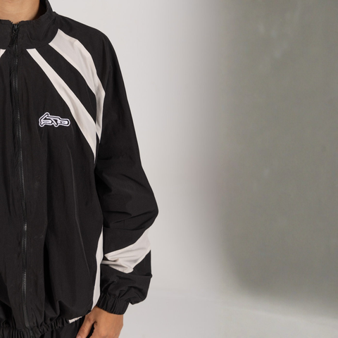 Model wearing the BROWNTOAST Compton Tracksuit Jacket — unisex oversized polyester track jacket with a dual-function zipper and BTO rubber and embroidered logos. Inspired by old-school Compton style and 80s hip-hop culture. Available in black and white.