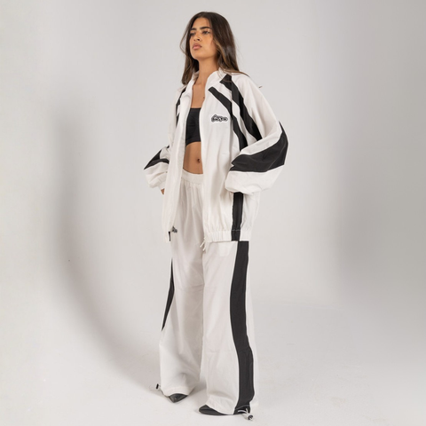 Model wearing the BROWNTOAST Compton Tracksuit Jacket — unisex oversized polyester track jacket with a dual-function zipper and BTO rubber and embroidered logos. Inspired by old-school Compton style and 80s hip-hop culture. Available in black and white.