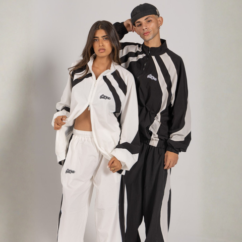 Model wearing the BROWNTOAST Compton Tracksuit Jacket — unisex oversized polyester track jacket with a dual-function zipper and BTO rubber and embroidered logos. Inspired by old-school Compton style and 80s hip-hop culture. Available in black and white.