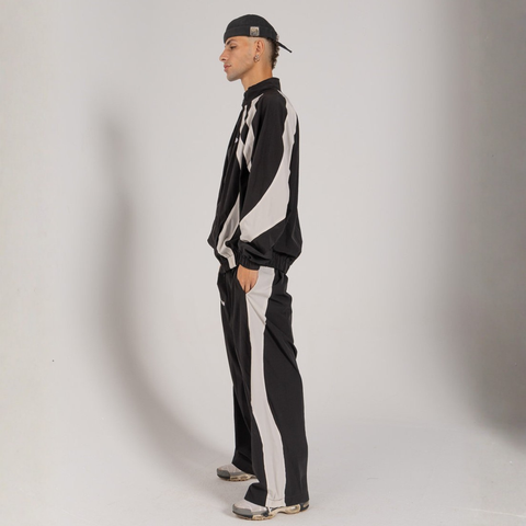 Model wearing the BROWNTOAST Compton Tracksuit Jacket — unisex oversized polyester track jacket with a dual-function zipper and BTO rubber and embroidered logos. Inspired by old-school Compton style and 80s hip-hop culture. Available in black and white.