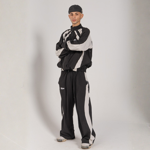 Model wearing the BROWNTOAST Compton Tracksuit Jacket — unisex oversized polyester track jacket with a dual-function zipper and BTO rubber and embroidered logos. Inspired by old-school Compton style and 80s hip-hop culture. Available in black and white.