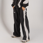 Model wearing the BROWNTOAST Compton Tracksuit Pants — unisex oversized polyester track pants inspired by old-school Compton style and 80s hip-hop culture. Features adjustable waist and BTO rubber and embroidered logos. Available in black and white.