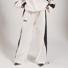 Model wearing the BROWNTOAST Compton Tracksuit Pants — unisex oversized polyester track pants inspired by old-school Compton style and 80s hip-hop culture. Features adjustable waist and BTO rubber and embroidered logos. Available in black and white.