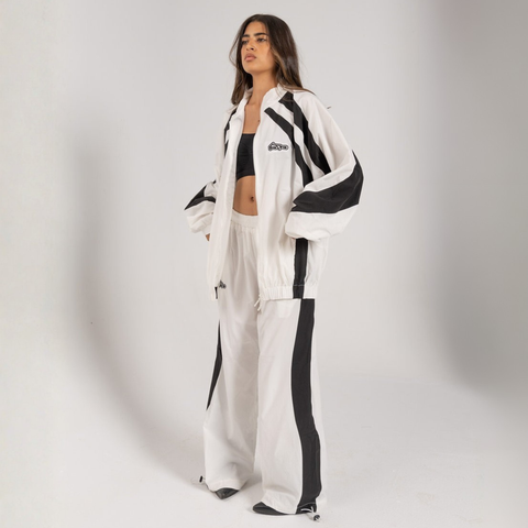 Model wearing the BROWNTOAST Compton Tracksuit Pants — unisex oversized polyester track pants inspired by old-school Compton style and 80s hip-hop culture. Features adjustable waist and BTO rubber and embroidered logos. Available in black and white.