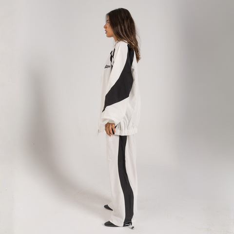 Model wearing the BROWNTOAST Compton Tracksuit Pants — unisex oversized polyester track pants inspired by old-school Compton style and 80s hip-hop culture. Features adjustable waist and BTO rubber and embroidered logos. Available in black and white.