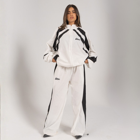 Model wearing the BROWNTOAST Compton Tracksuit Pants — unisex oversized polyester track pants inspired by old-school Compton style and 80s hip-hop culture. Features adjustable waist and BTO rubber and embroidered logos. Available in black and white.