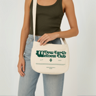 Limited edition canvas crossbody bag in beige featuring side pocket, inner compartments, and front and back design in dark green.